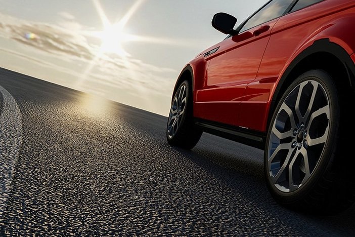 Your Car Is an Expensive, Health-Sucking, Time-Wasting Machine. So, Ditch It! brand new red sedan driving on dark pavement with sunbeam ahead in partly cloudy sky