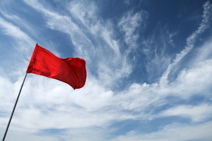 3 Pre-Inspection Red Flags That Make Me Run From a Deal blue sky background with some clouds and red flag in foreground waving in wind