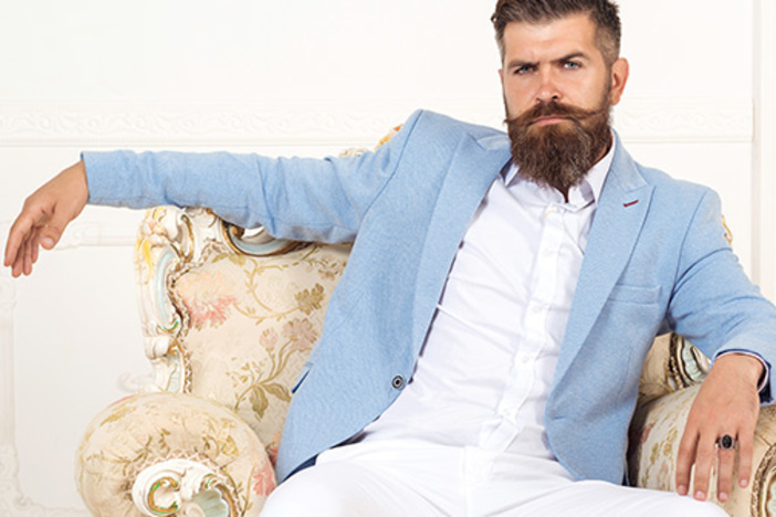 This Is the Best Way to Become A Millionaire Through Real Estate Investing Successful young bearded elegant businessman in suit with perfect hairstyle indoors, relaxing, sits on arm chair, looks harsh and virile. Rich man wearing blue jacket and white pants. Fashion concept