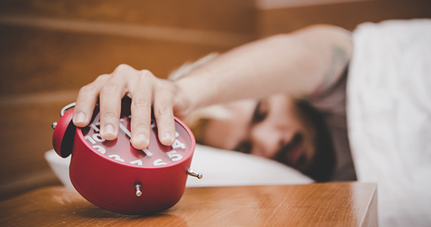 How to Wake Up Earlier (& Actually Love It) in 5 Simple Steps Young sleepy man trying to turns off the alarm clock waking up at morning