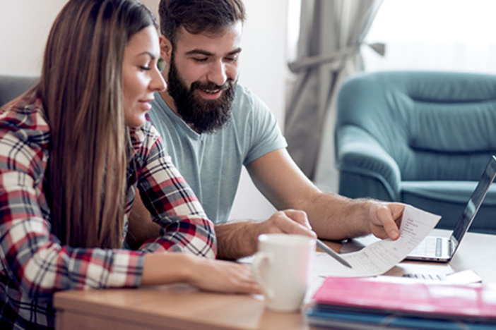Extreme Budgeting Tips: Save Up a Down Payment Fast Young couple using a computer,checking bills and paperwork.