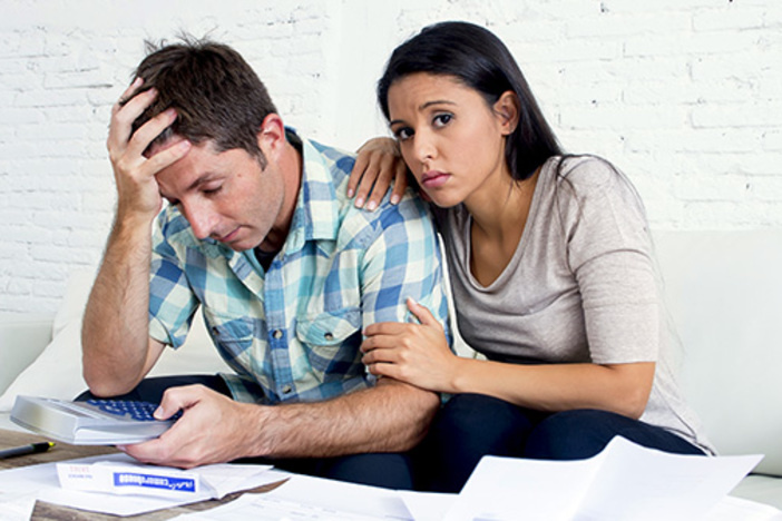 Stop Living Paycheck to Paycheck—Here’s How young sad couple at home living room couch calculating monthly expenses worried
