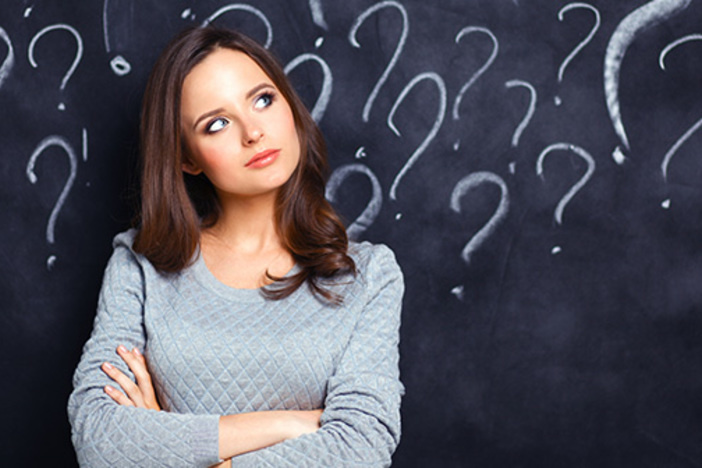 Think Cost Segregation Is Too Expensive? Here’s Why You’re Wrong young dark-haired woman in gray sweater standing in front of blackboard with questions drawn on it in white chalk