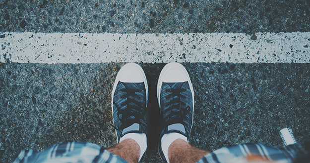 Neighborly Disputes: How to Handle Property Line Issues View of feet of guy in white socks and sneakers standing near grunge white line on asphalted road, ready to pass