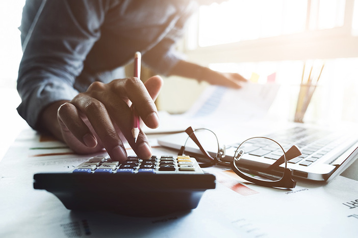 The 1% Rule in Real Estate: Is This a Realistic Way to Evaluate Rentals? Close up of businessman or accountant hand holding pen working on calculator to calculate business data, accountancy document and laptop computer at office, business concept