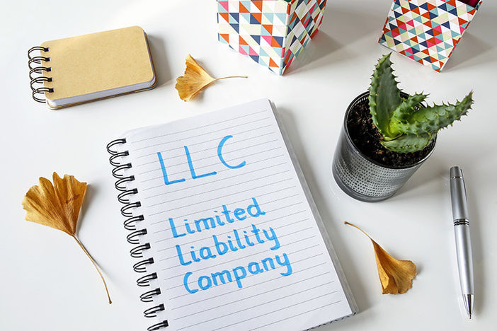Do Landlords Need an LLC for Rental Property? LLC written in blue marker on a spiral notebook laying on desk with small potted plant and other desk decor