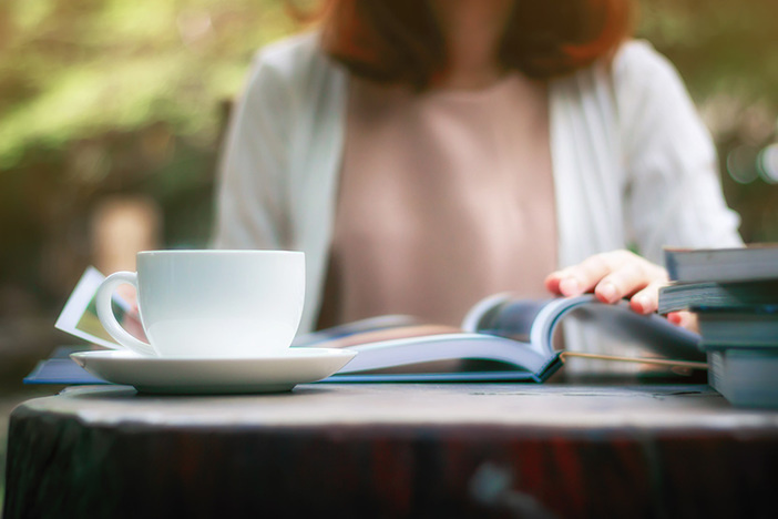 New to Investing? Read These 10 Real Estate Books (In This Order!) Close up of woman reading a book and drinking coffee in the garden.