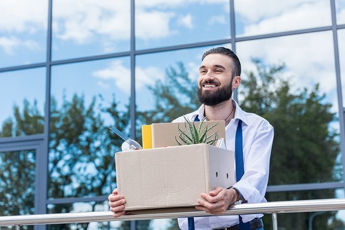 The First (and Most Critical) Step to Passive Real Estate Investing happy businessman with cardboard box with office supplies in hands standing outside office building, quitting job concept