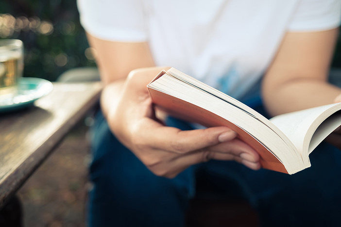 5 Business Books That Changed My Real Estate Investing Life closeup of man in white shirt and blue jeans sitting and reading a paperback book