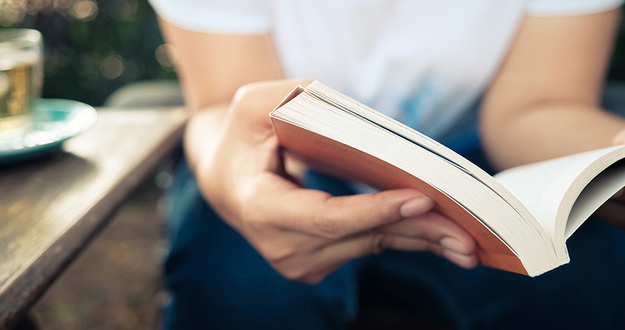 5 Business Books That Changed My Real Estate Investing Life closeup of man in white shirt and blue jeans sitting and reading a paperback book