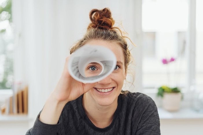 5 Deal-Finding Tricks I Use to Buy Around 100 Properties a Year Young woman playing I spy with the camera looking through a rolled cylinder of paper with one eye and a happy smile