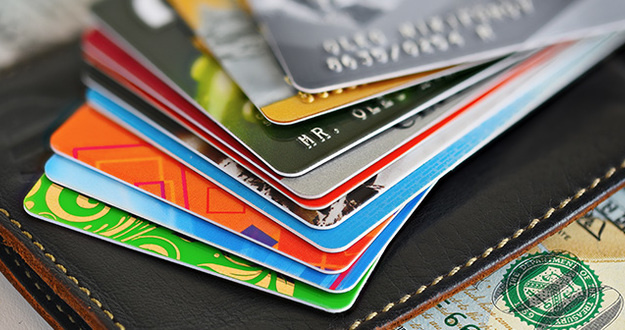 How to Choose the Smartest Credit Cards to Use for Your Spending Habits closeup of tabletop with pile of fanned credit cards on wallet on cash
